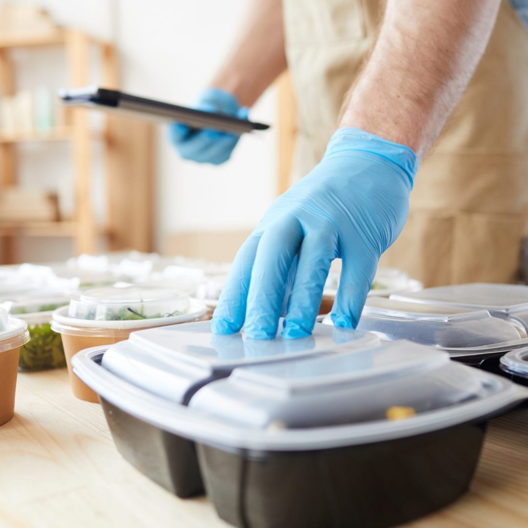 Close-up of delivery person in protective gloves preparing food in boxes for delivery